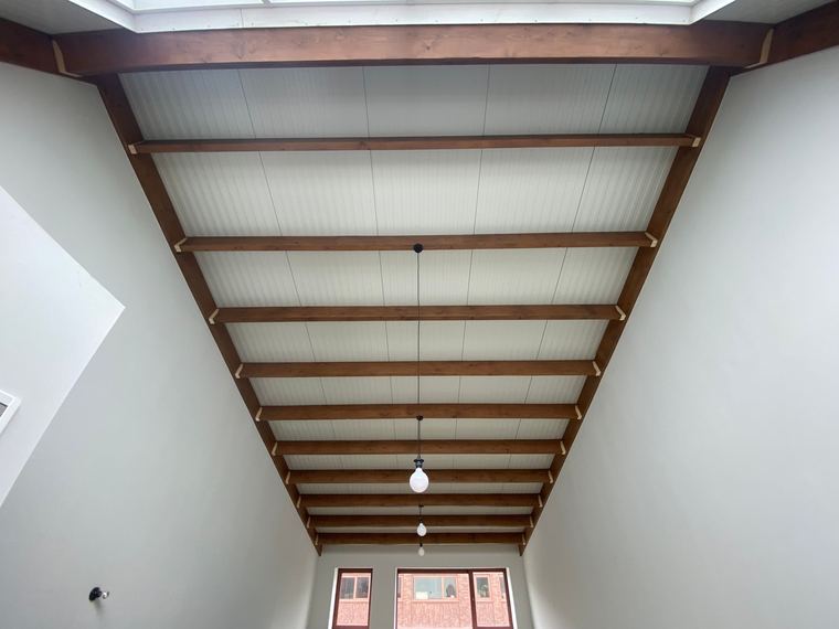 Wit geschilderd plafond tussen gebeitste houten balken in een aanbouw
