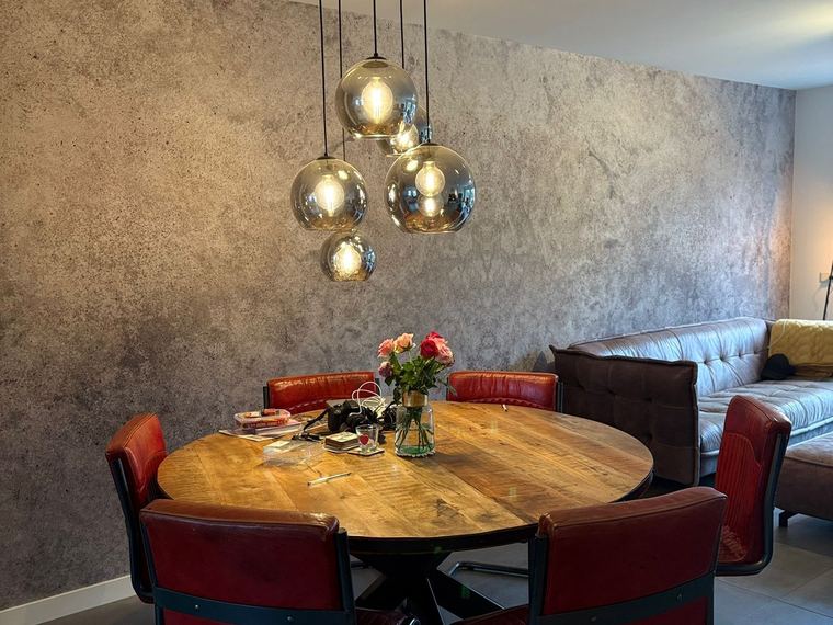 Eetkamer met betonlook-wand in warme grijstinten onder een cluster hanglampen