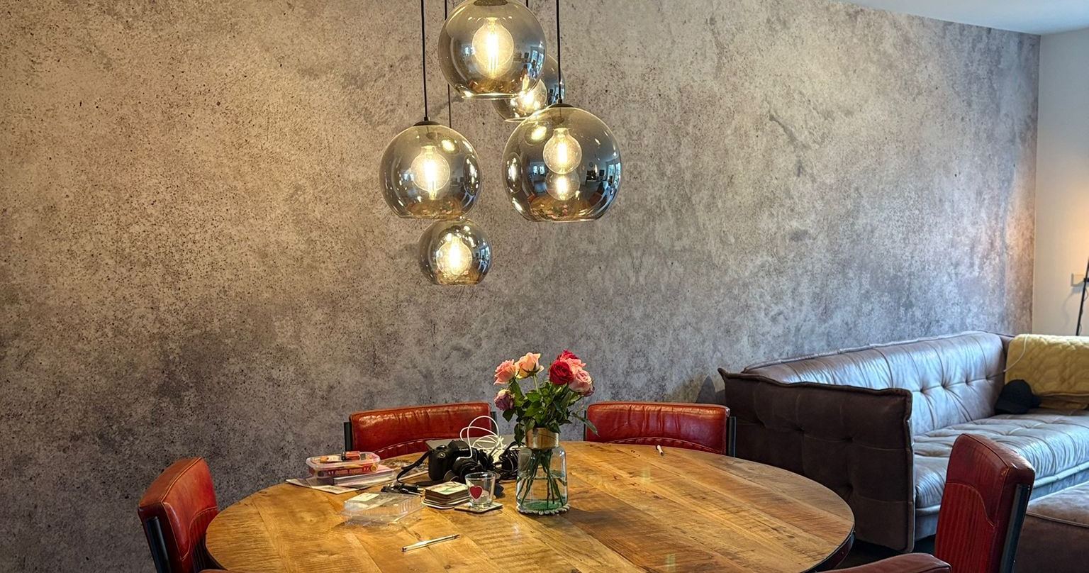 Eetkamer met een strak gestucte betonlook-wand, afgewerkt door A.J. Klus & Afwerking